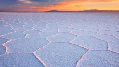 Salar de Uyuni, eine weite, flache Salzfläche mit großen, sechseckigen Mustern unter einem farbenfrohen Sonnenuntergang am Horizont.