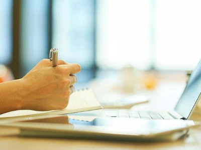 Eine Hand die schreibt mit Computer daneben