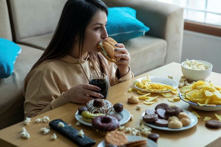 Woman eating a sandwich in front of a messy table full of junk food
