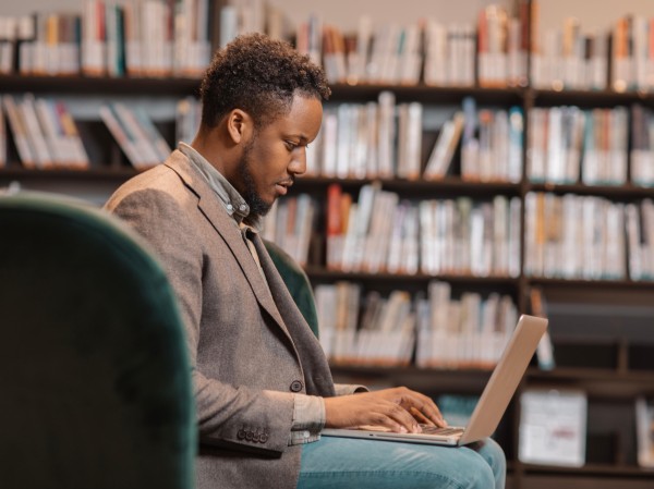 A male scientist is sat in a chair looking at his laptop