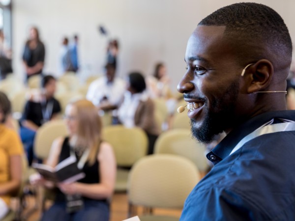 A middle-aged male speaker smiles at an unseen person as he prepares to address the Expo audience.