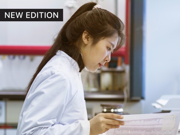 female researcher in a labcoat, at a desk looking concentrated, reviewing papers