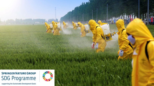 farmers spraying pesticide in wheat field wearing protective clothing