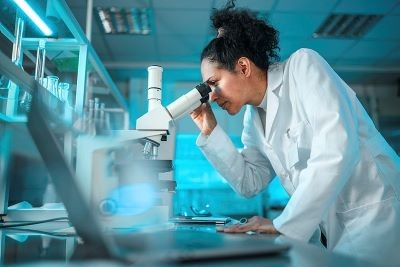Female Scientist in lab looking down microscope.