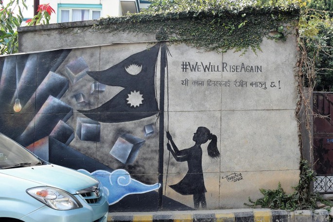 A photograph of a mural displays a little girl raising a Nepal flag. The text above reads, number sign, We Will Rise Again.