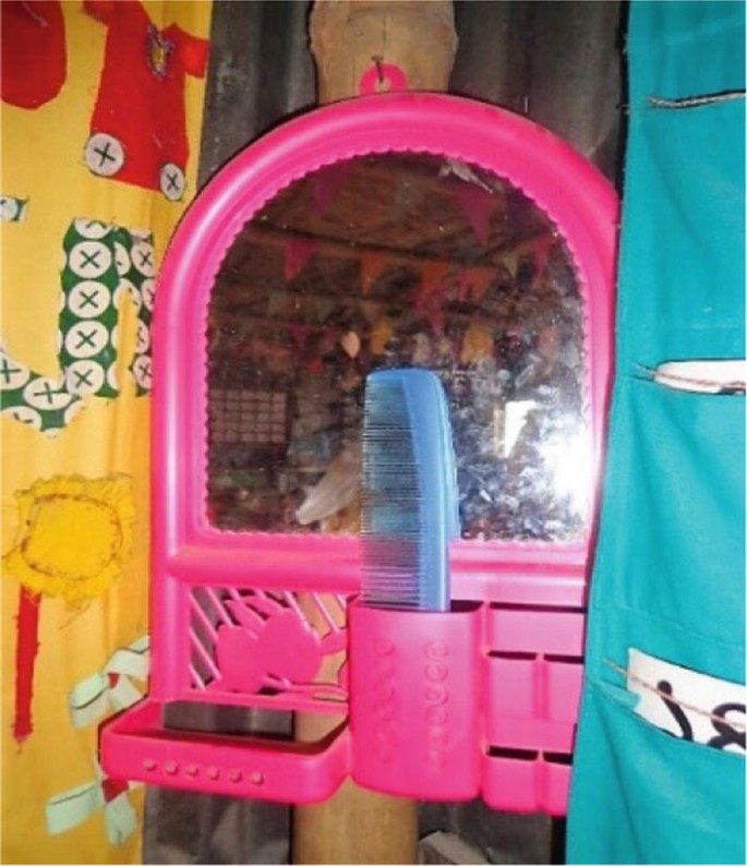 A photograph captures a small mirror, hanging off of a nail. There is a comb in one of the mirror's holders.