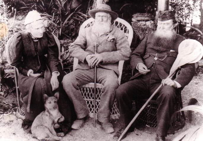 A grayscale view of Mary Elizabeth Barber seated with Thomas Holden Bowker, and James Henry. Both men have sticks in their hands. A dog sits near Mary Elizabeth Barber.