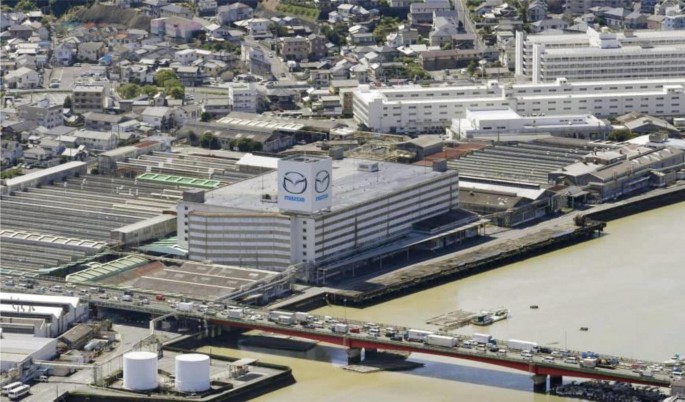 A top-view of a large rectangular building near a water body. The bridge and other buildings are near it.