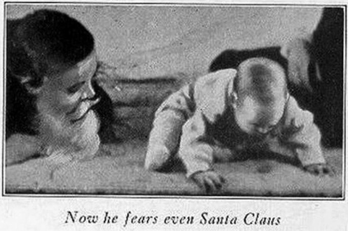 A photograph of a little child bending over to look for something on the floor. A woman by the side bends and watches over. The caption reads, now he fears even Santa Claus.