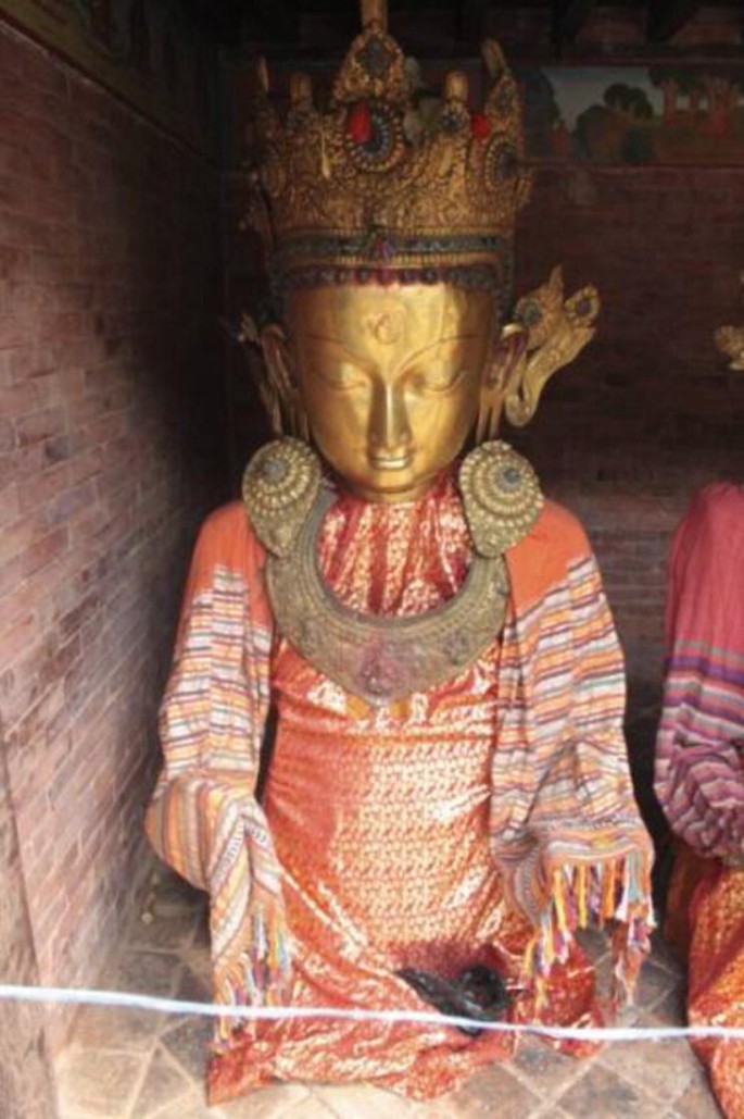 A statue of the Buddha decorated with a copper mask, crown, and a heavy necklace.