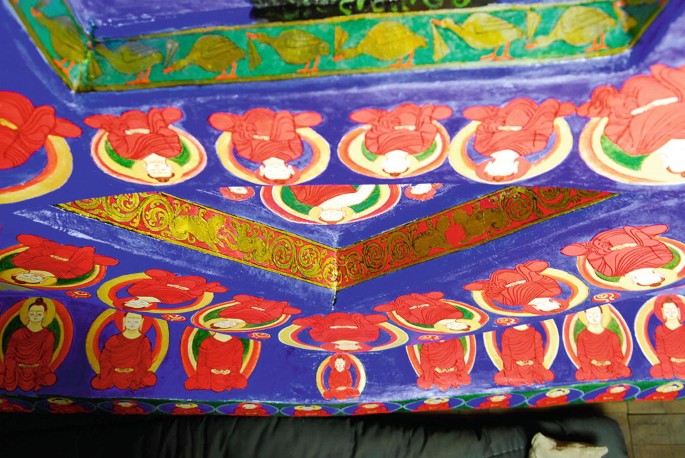 A close-up photograph of the painting depicts Buddha figures, arabesque patterns, and animal motifs.