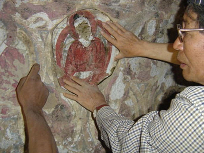 A photograph of Professor Kosaku Maeda placing a photocopy of a wall painting fragment on the wall from where it was looted.