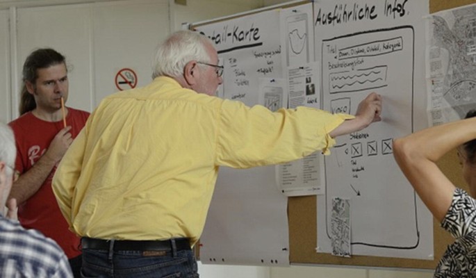 A photo of a group of people examining a route on a map, which is posted on a board.