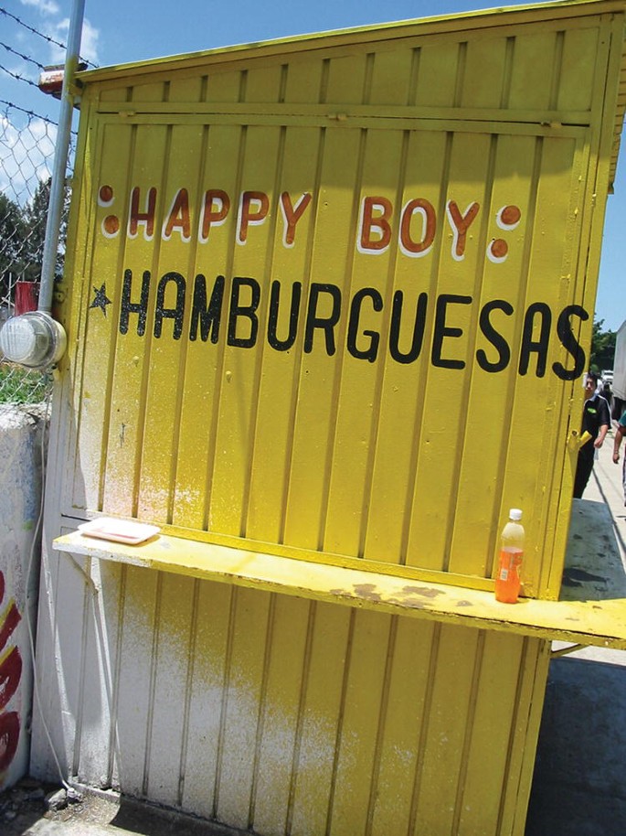 A photograph of a sidewalk stand that has Happy boy Hamburguesas written on it.