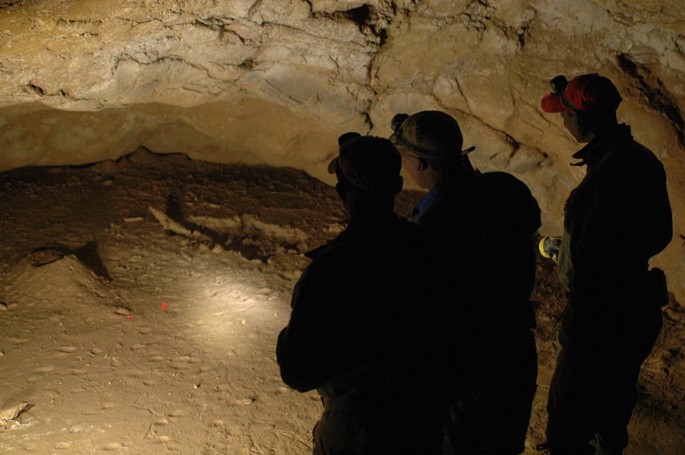 A photograph of 3 people in a cave who search for something with light.