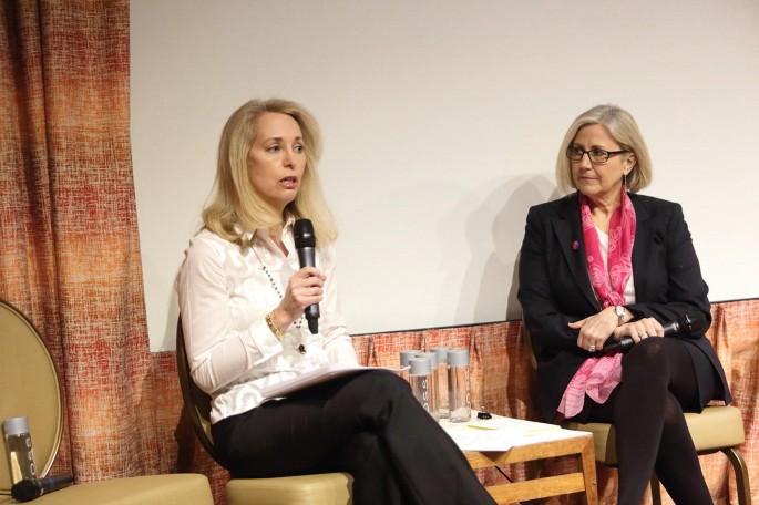 A photo of Valerie Plame Wilson and Kate Folb seated with their legs crossed. Both have a microphone in their hands.