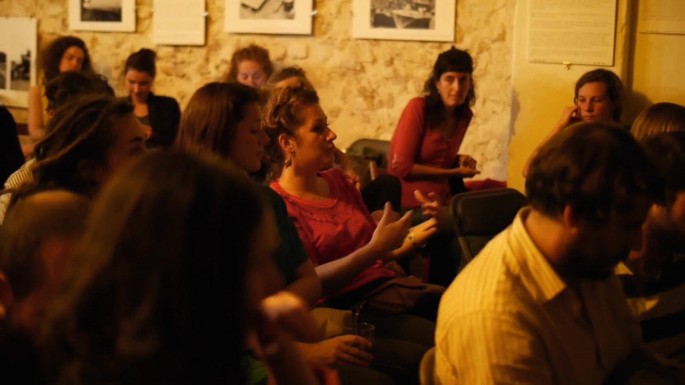 A group of men and women are seated in chairs. A woman in the center is in the middle of speaking something.