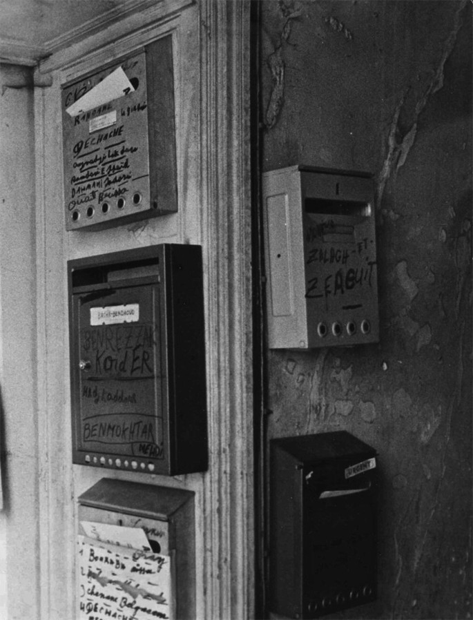 A grayscale view of a two-sided wall. The left face has three mailboxes stacked one above the other. The right face has two similar stacked-up mailboxes.