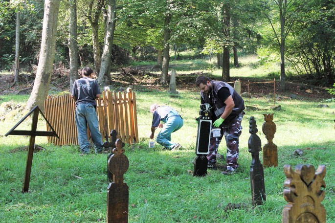 Photograph of a group of people renovating grave markers made of wood in a burial ground.