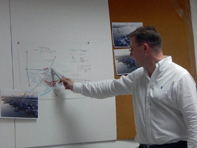A photograph of a person explaining a process with the help of a chart and three landscape photographs.