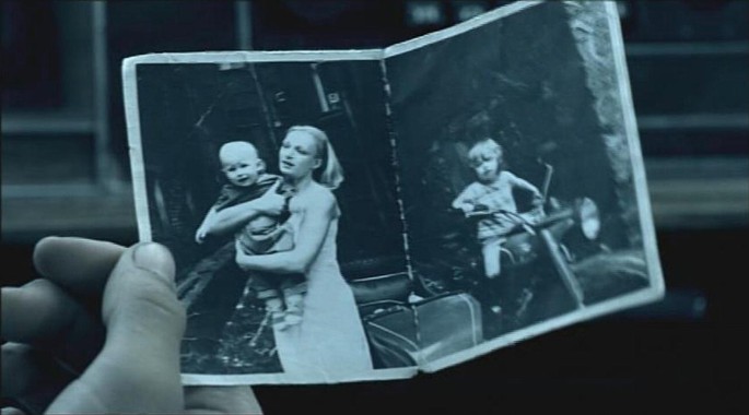 A screen capture from the movie, The Return. One of the two sons is holding a photograph of the mother holding the younger brother Vanya, while the older brother Ivan, is on a motorbike.