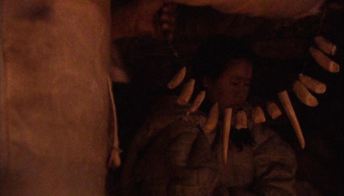 A screen capture from the movie, Atanarjuat. It is of the moment where the walrus necklace, that the shaman is taking to give to the son, frames Panipak.