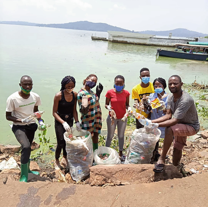A photograph of a group of young people collecting plastic garbage from a river bank.
