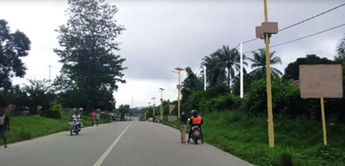 An image of a street with utility poles. Some people drive on the road.