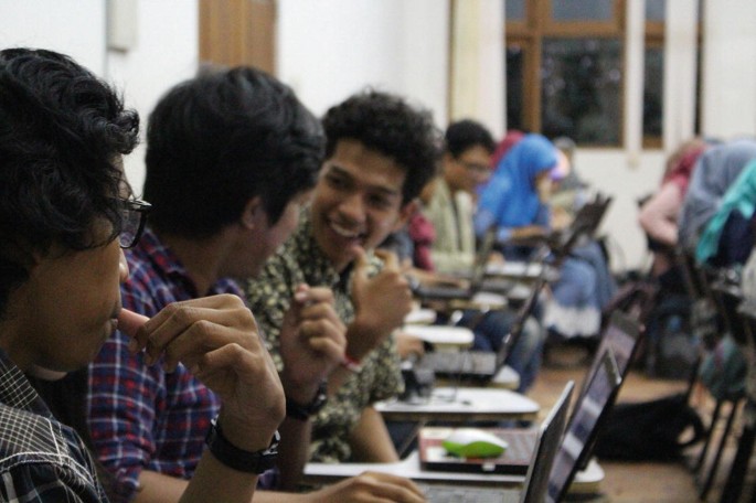 A photograph depicts students in a classroom with laptops to trace the building data around Mount Sinabung.