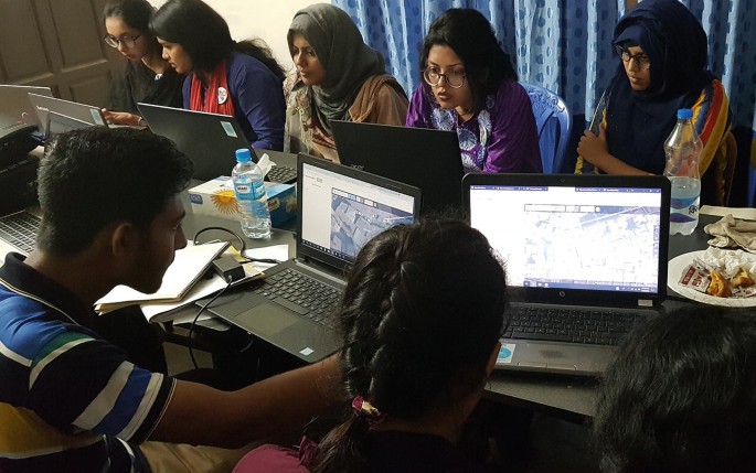 A photograph depicts a group of students in a room mapping data on laptops.