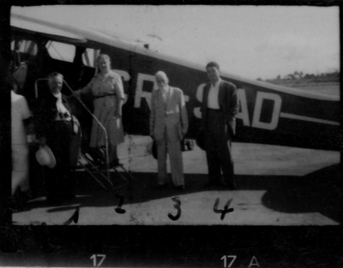 A photograph of 3 men and a woman standing outside an airplane before boarding.