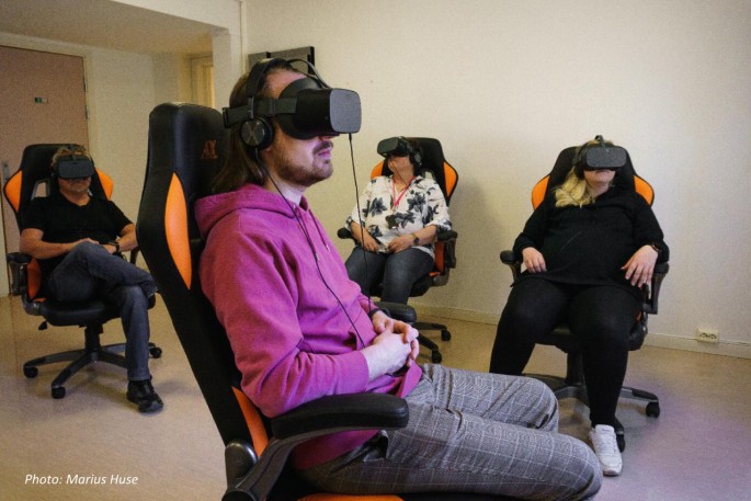 Four people sitting on chairs wearing V R glasses.