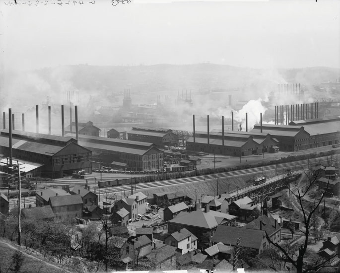 A photo of a steelwork factory with buildings, chimney outlets and smoke covering the area.