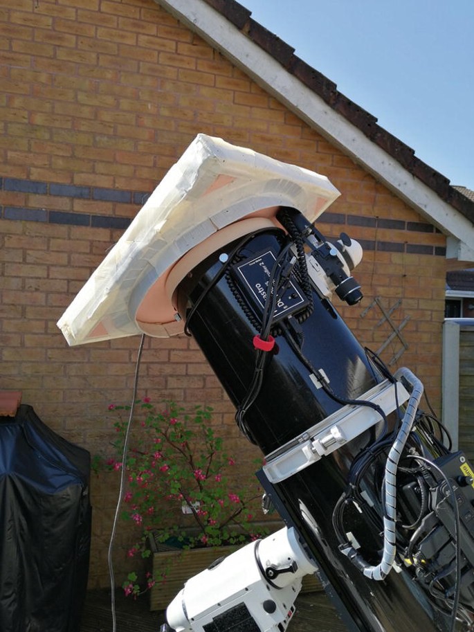 A photograph of a sky flat light box setup on aopen area. The tip of the dew shield of the sky flat is covered with a rectangular-shaped object.