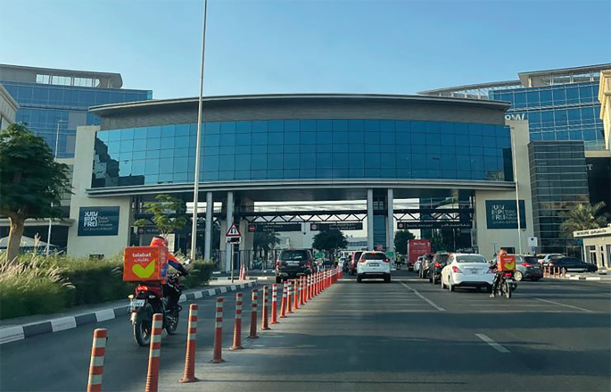 A photograph of the Dubai Airport free zone, with some vehicles approaching a toll under a glass-walled building.