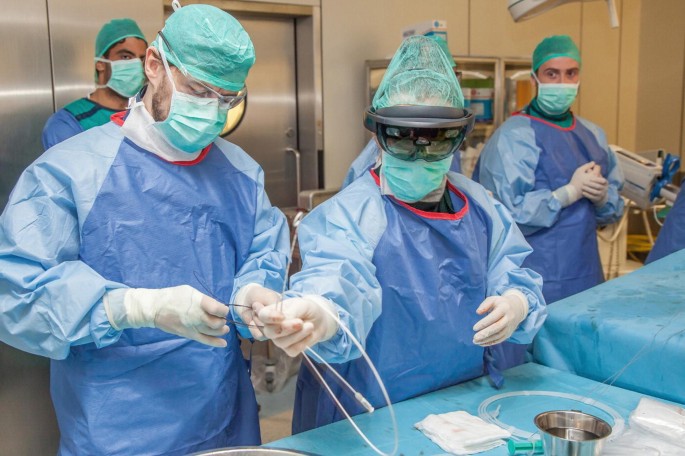 A photograph depicts the two doctors, who wear gloves, masks, and glasses with tubes on their hands, and two people standing behind them.