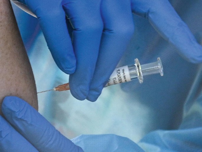 A photograph of a healthcare officer pushing an injection into a person.