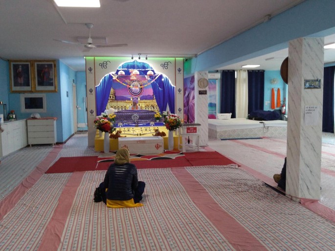 A photo of the prayer hall in the Italian gurdwara where a few devotees sit on the floor.