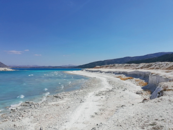 A photograph of Salda lake with the deposits of minerals located on Beyaz Adalar Beach. The sediment resembles salt in color and graininess.