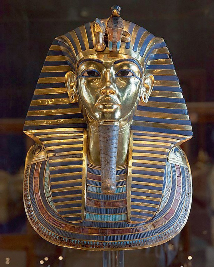 A photograph of the Egyptian funerary mask. It is made of gold, and semi-precious stones. It has a sculpture of a snake on the crown.