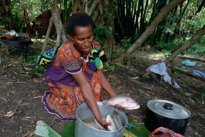A photograph of a person who takes out fish from a vessel full of fish.