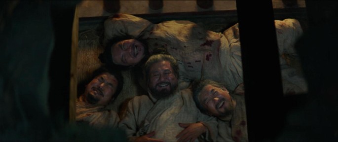 A top-view photograph of 4 Chinese men lying on a wooden bed and staring at the sky through an opening in the roof. They have wide smiles on their faces.