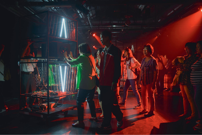 A photograph with people viewing an opera performed by a robot inside a glass case.