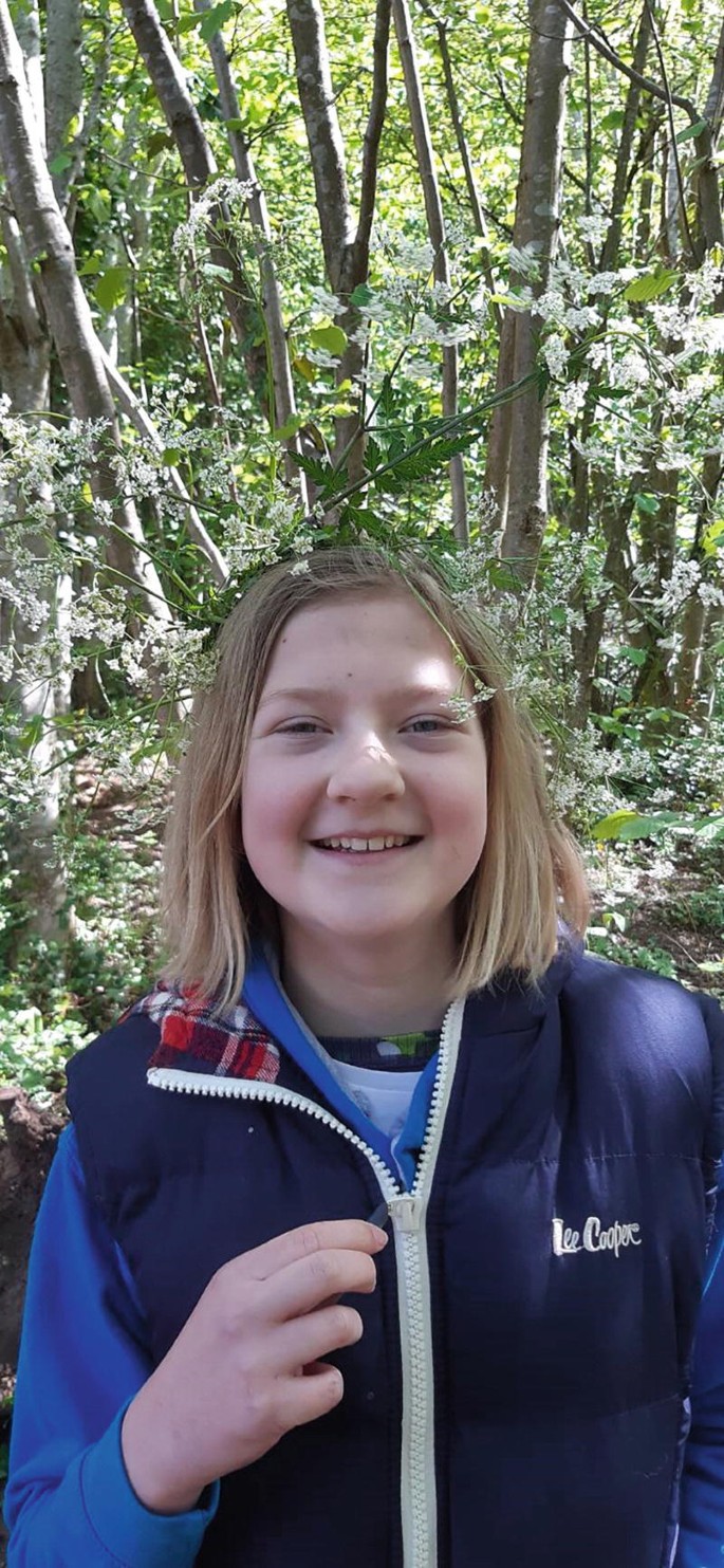 A photograph of a girl who stands in the middle of a forest and smiles.