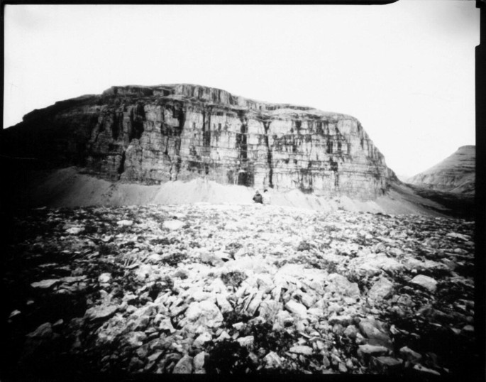 A photograph of a barren land with a lot of rocks and a cliff in the background.