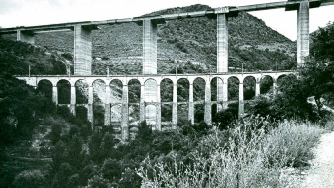 A photograph of a dam. The infrastructure of a dam is surrounded by green valleys.