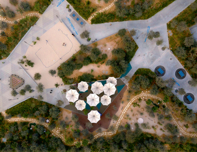 A satellite view of a park with a shaded umbrella for seating, playgrounds, and pathways surrounded by greenery.