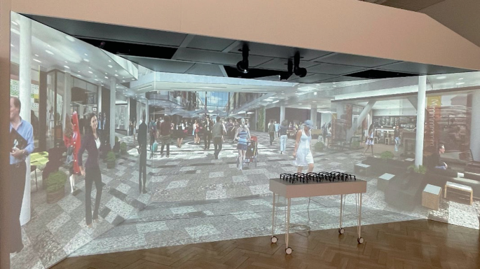 A photograph of a virtual 3-D environment. It depicts a virtual cave view with people roaming and sitting in a public area.