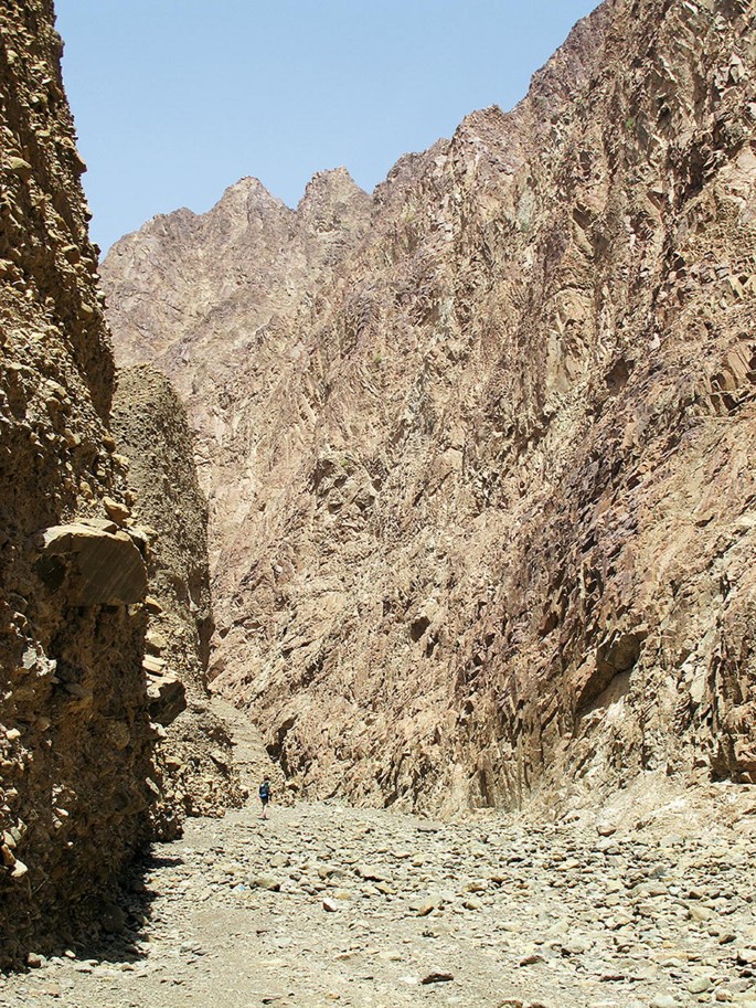 A photograph of a rocky terrain with a narrow pathway winding through it. The pathway is surrounded by tall, rugged cliffs and boulders.