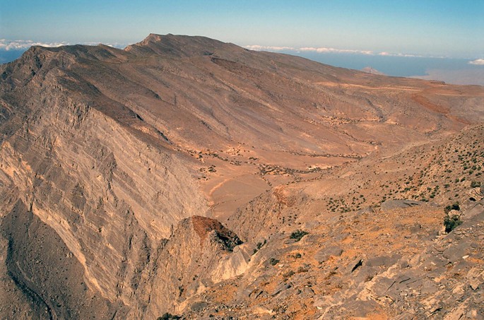A photograph of a mountainous terrain with steep cliffs and rocky outcroppings. The sky is clear and blue, and there are no visible signs of life or vegetation.